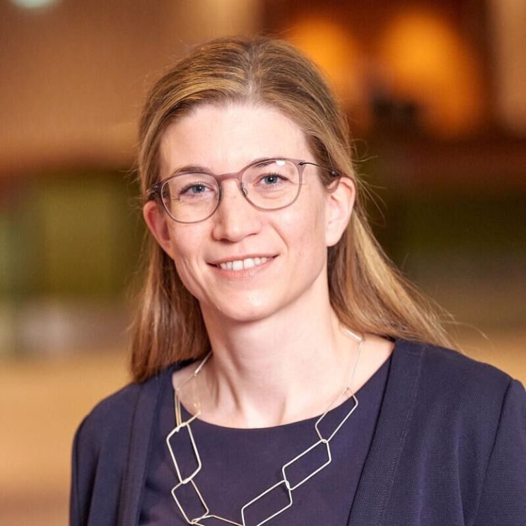 Eine lächelnde Frau mit langen braunen Haaren trägt ein dirndlähnliches Outfit.